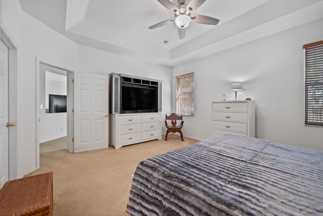 bedroom with light colored carpet, baseboards, a tray ceiling, and a ceiling fan