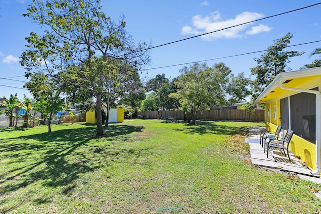 view of yard with an outbuilding, a fenced backyard, a storage shed, and a sunroom