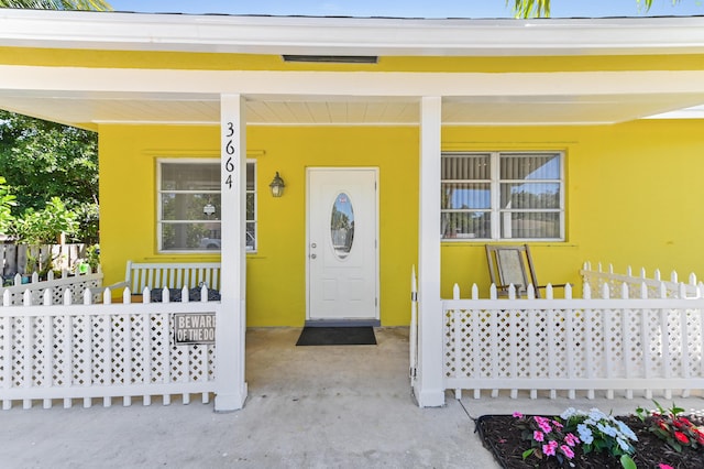 view of exterior entry with fence, covered porch, and stucco siding