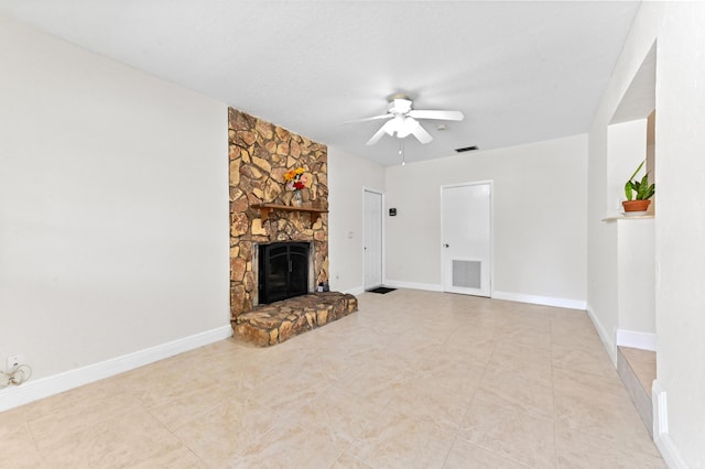 unfurnished living room featuring a stone fireplace, a ceiling fan, visible vents, and baseboards