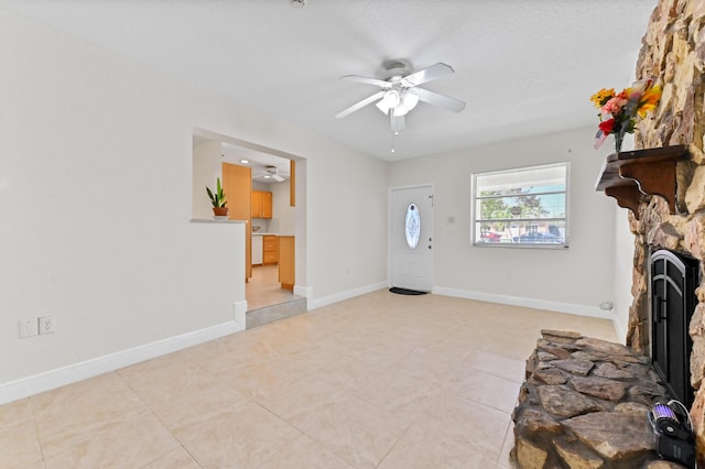 entrance foyer with light tile patterned floors, a stone fireplace, baseboards, and ceiling fan