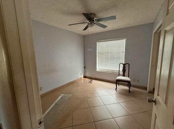 interior space with baseboards, a textured ceiling, ceiling fan, and tile patterned flooring