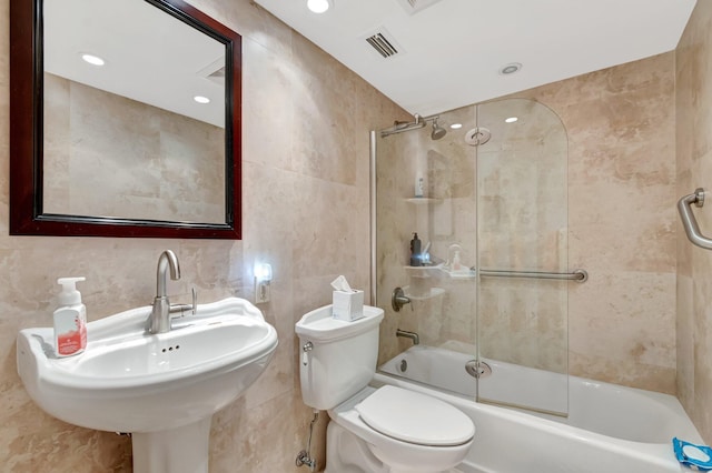 bathroom with visible vents, shower / bath combination with glass door, a sink, tile walls, and toilet