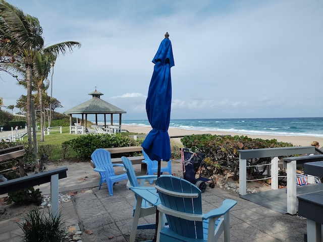 view of patio / terrace featuring a gazebo, an outdoor fire pit, a view of the beach, and a water view