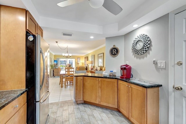 kitchen featuring visible vents, ceiling fan with notable chandelier, dark stone countertops, freestanding refrigerator, and a peninsula