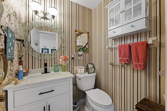 bathroom featuring toilet, vanity, and wallpapered walls