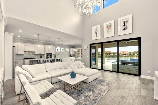 living room with baseboards, an inviting chandelier, recessed lighting, ornamental molding, and light wood-type flooring