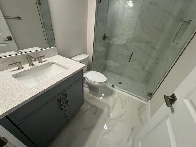 bathroom featuring vanity, toilet, marble finish floor, and a marble finish shower