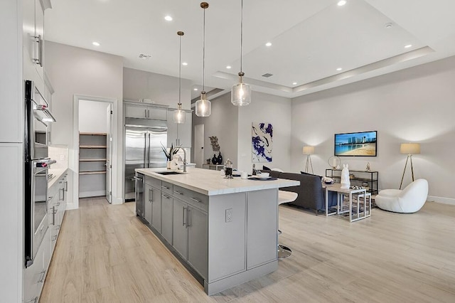 10097 Driftwood Way, Palm Beach Gardens, FL 33412 - kitchen featuring a kitchen island with sink, appliances with stainless steel finishes, gray cabinetry, a sink, and light wood finished floors