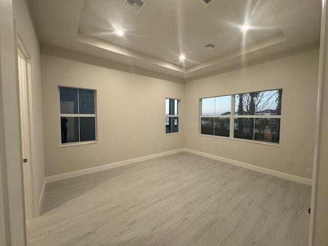 empty room with a tray ceiling, baseboards, visible vents, and wood finished floors