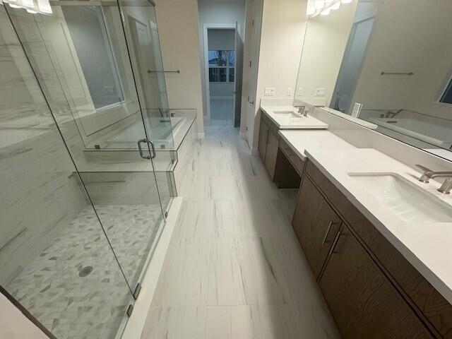 full bathroom with a sink, a marble finish shower, and double vanity