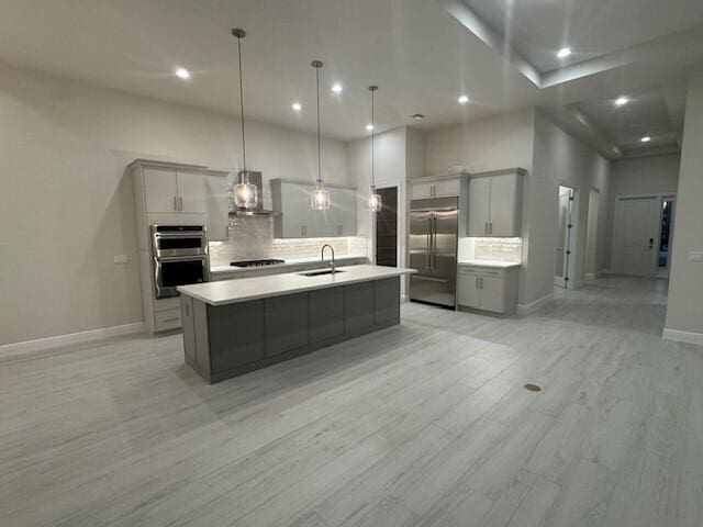 kitchen featuring gray cabinetry, a sink, tasteful backsplash, stainless steel appliances, and wall chimney range hood