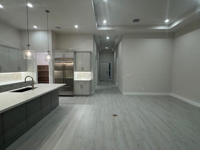 kitchen with gray cabinetry, light wood-style flooring, a sink, built in fridge, and light countertops