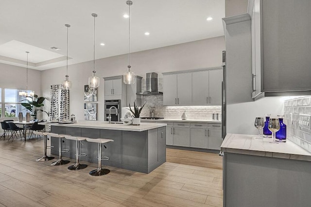 10097 Driftwood Way, Palm Beach Gardens, FL 33412 - kitchen with light wood-type flooring, decorative backsplash, wall chimney exhaust hood, and gray cabinetry