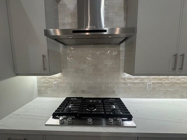 interior details featuring decorative backsplash, gas cooktop, light stone countertops, and wall chimney range hood