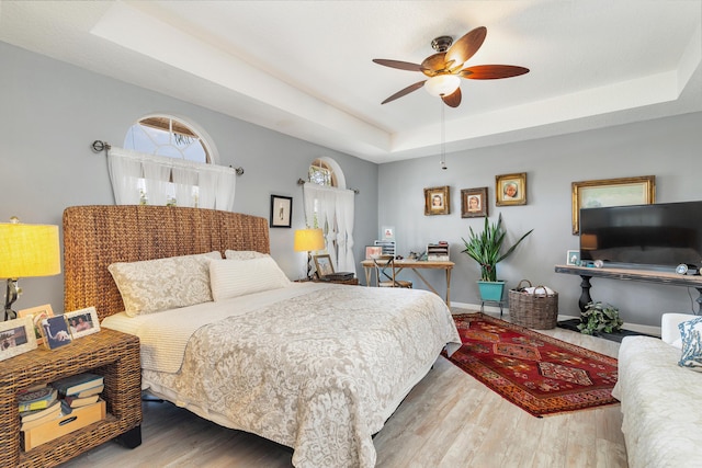 bedroom featuring a raised ceiling, wood finished floors, baseboards, and a ceiling fan