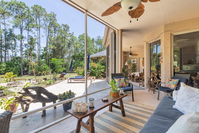 sunroom / solarium with a ceiling fan, an outdoor living space, and view of wooded area