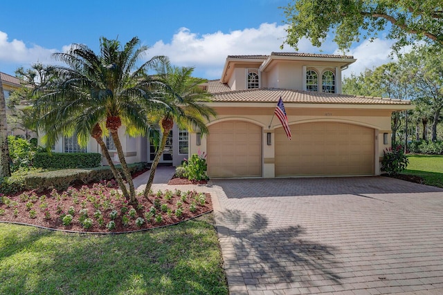 mediterranean / spanish home with a tile roof, decorative driveway, an attached garage, and stucco siding