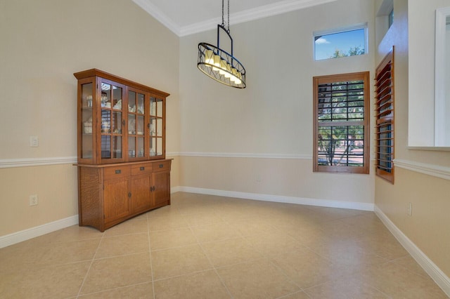 unfurnished dining area featuring crown molding, a high ceiling, light tile patterned floors, and baseboards