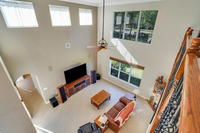 living area with visible vents, baseboards, a high ceiling, arched walkways, and a ceiling fan