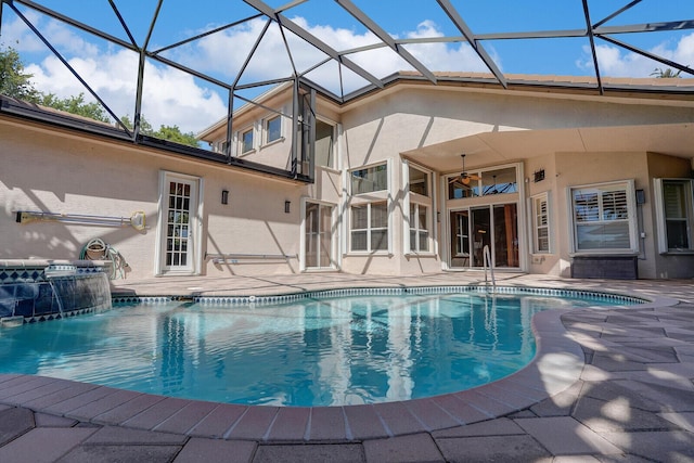 outdoor pool with glass enclosure, a patio area, and ceiling fan