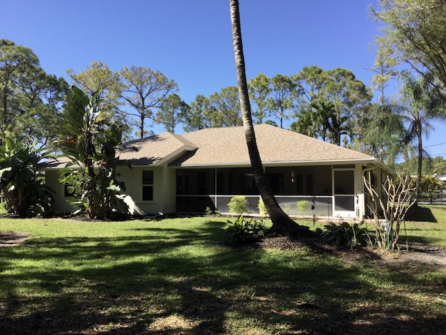 rear view of house with stucco siding, a lawn, roof with shingles, and a sunroom