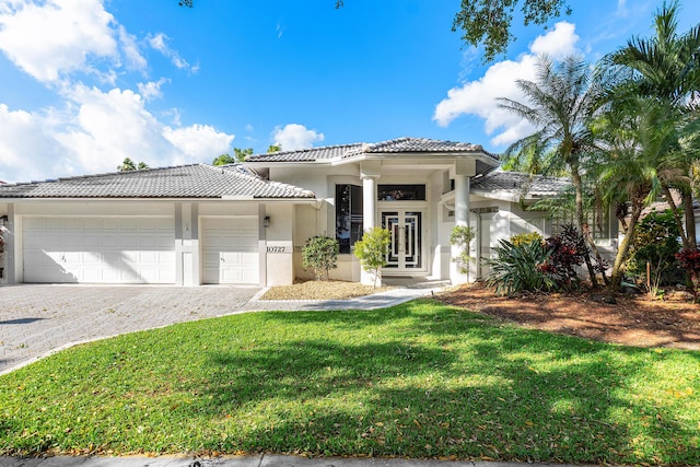 view of front facade featuring a tiled roof, a front yard, stucco siding, decorative driveway, and an attached garage