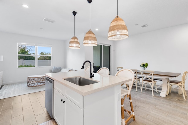 kitchen featuring a kitchen island with sink, a sink, light countertops, white cabinets, and stainless steel dishwasher