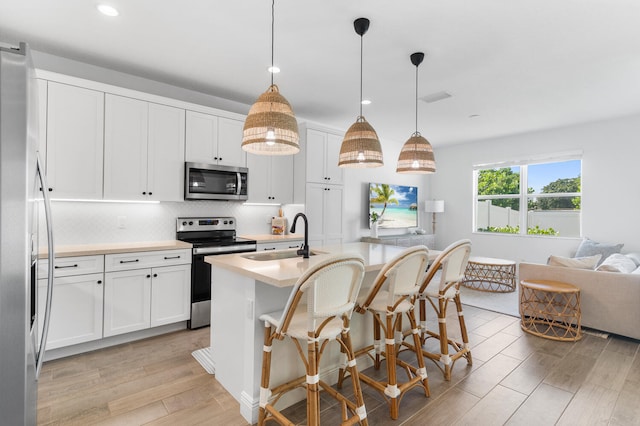 kitchen with a sink, decorative backsplash, light countertops, light wood-style floors, and appliances with stainless steel finishes