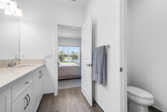 bathroom with baseboards, toilet, ensuite bathroom, wood finished floors, and vanity