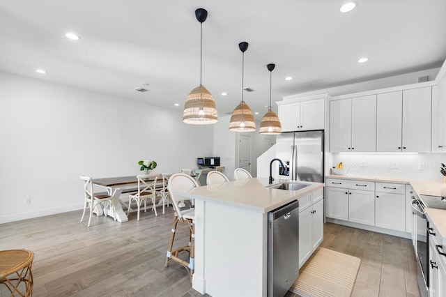 kitchen with a sink, light countertops, appliances with stainless steel finishes, tasteful backsplash, and light wood-type flooring