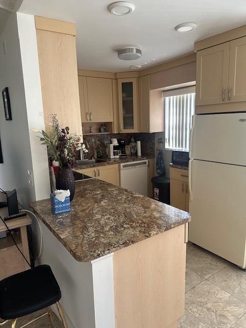 kitchen featuring white appliances, dark stone countertops, a peninsula, glass insert cabinets, and tasteful backsplash