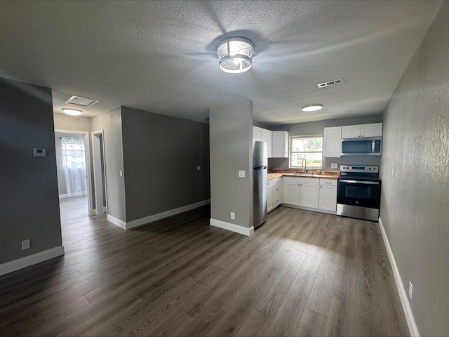 kitchen featuring dark wood finished floors, a sink, stainless steel appliances, a textured ceiling, and white cabinetry