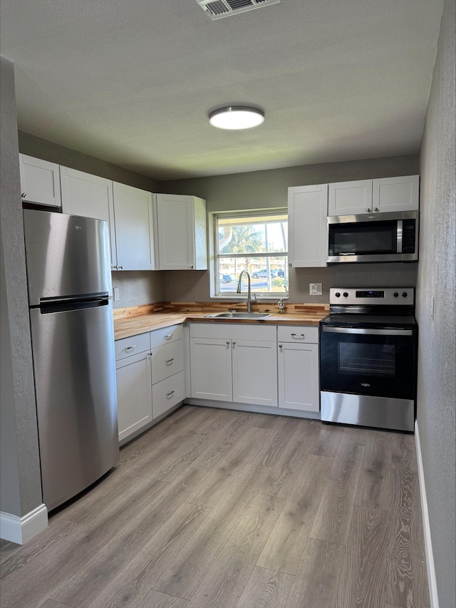 kitchen featuring a sink, stainless steel appliances, white cabinets, butcher block counters, and light wood finished floors