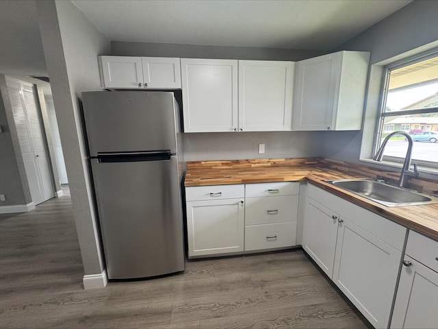 kitchen with a sink, white cabinets, butcher block counters, and freestanding refrigerator