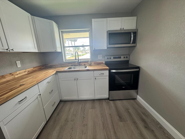 kitchen featuring baseboards, wooden counters, dark wood-style flooring, a sink, and appliances with stainless steel finishes