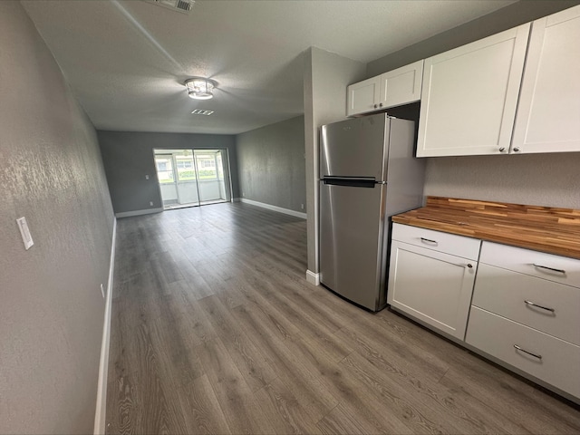 kitchen featuring wood finished floors, open floor plan, white cabinetry, freestanding refrigerator, and wooden counters