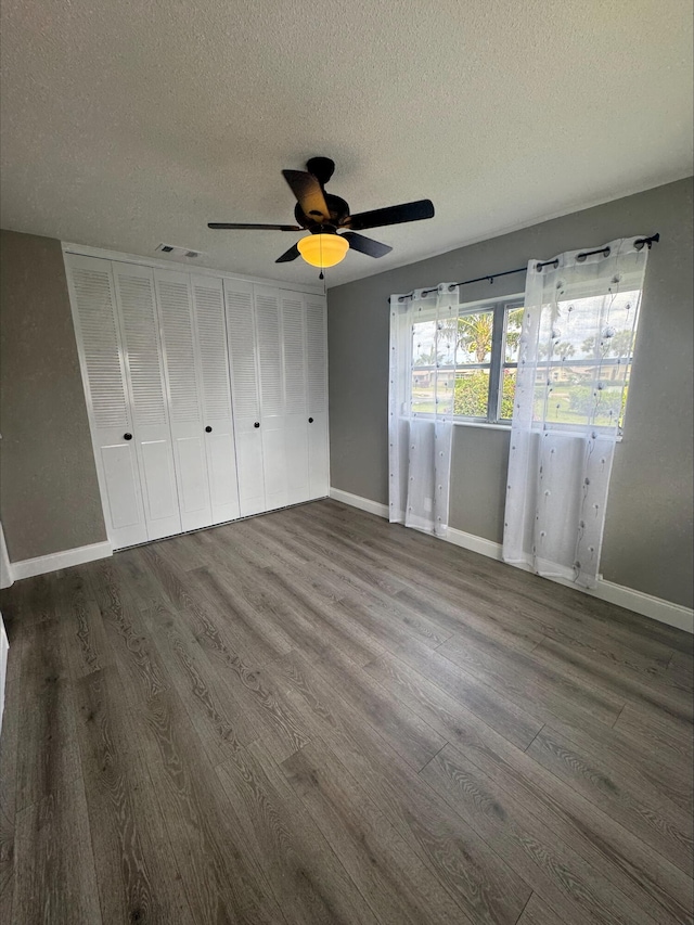 unfurnished bedroom featuring visible vents, dark wood-type flooring, a ceiling fan, a textured ceiling, and baseboards