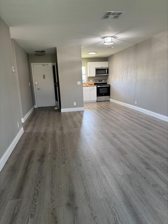 unfurnished living room with a textured ceiling, wood finished floors, visible vents, and baseboards