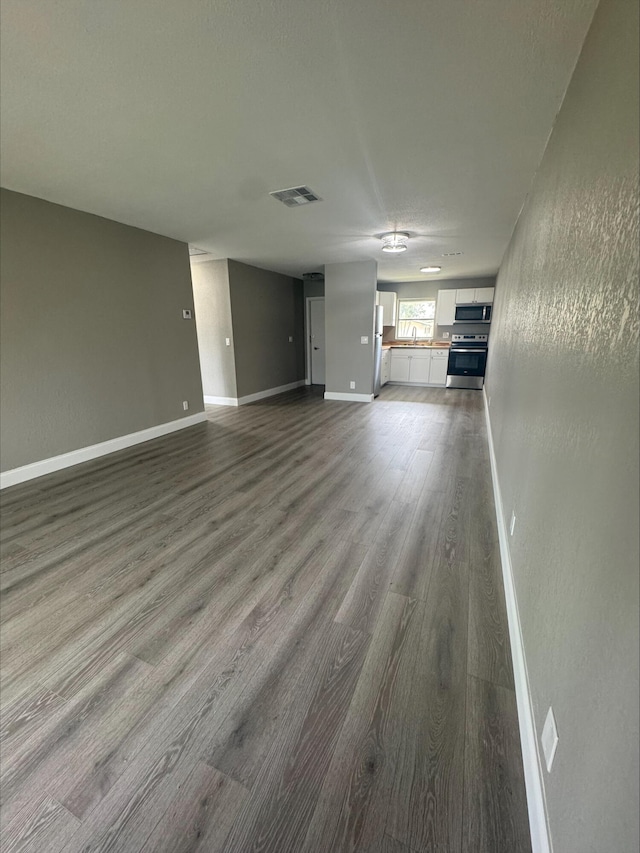 unfurnished living room featuring dark wood-style floors, visible vents, baseboards, and a textured wall