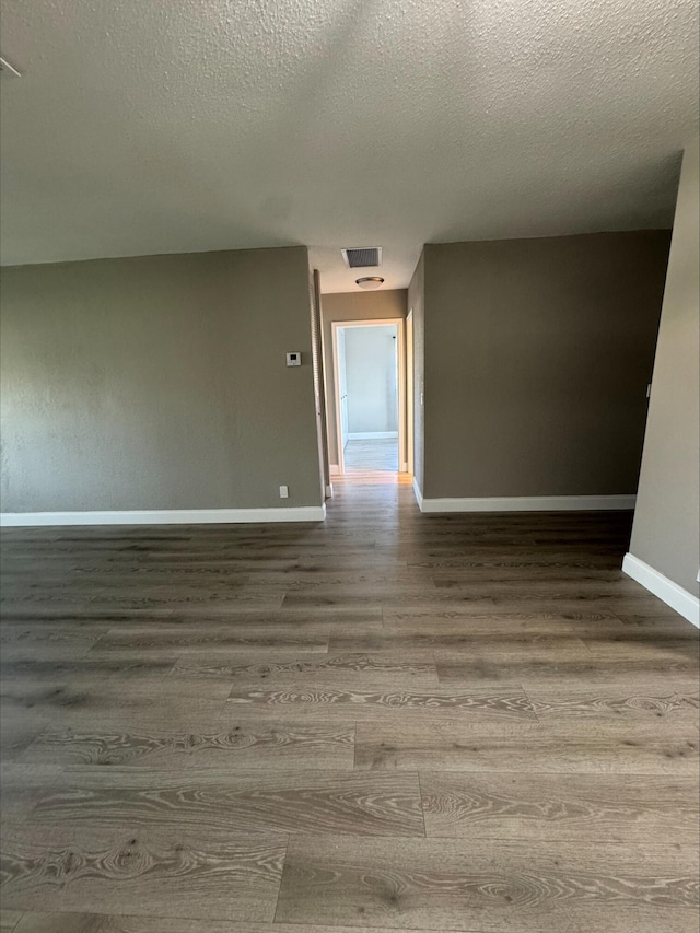 spare room with visible vents, baseboards, a textured ceiling, and wood finished floors