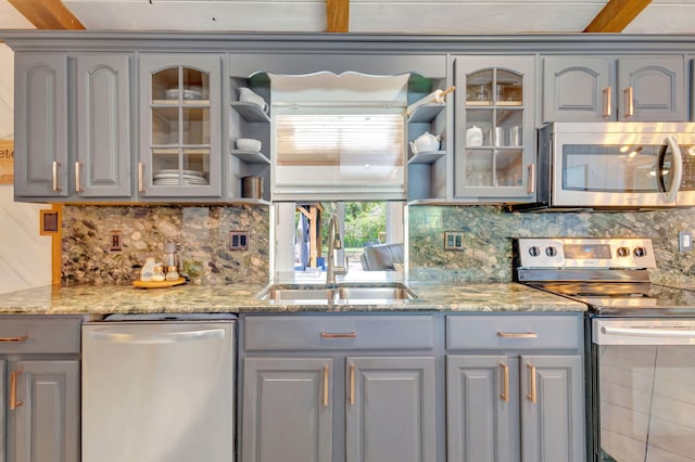 kitchen with gray cabinets, appliances with stainless steel finishes, glass insert cabinets, and a sink