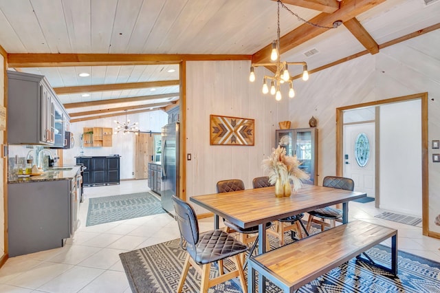 dining space featuring an inviting chandelier, lofted ceiling with beams, light tile patterned floors, and wood walls