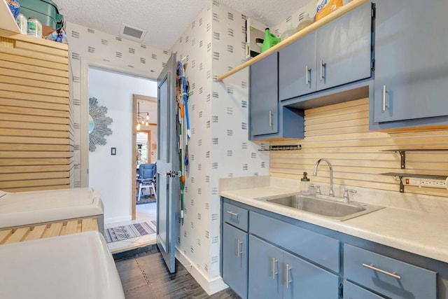 kitchen featuring wallpapered walls, a textured ceiling, blue cabinets, and a sink