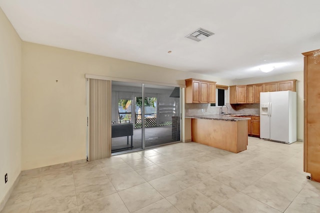 kitchen featuring tasteful backsplash, visible vents, a peninsula, white fridge with ice dispenser, and a sink