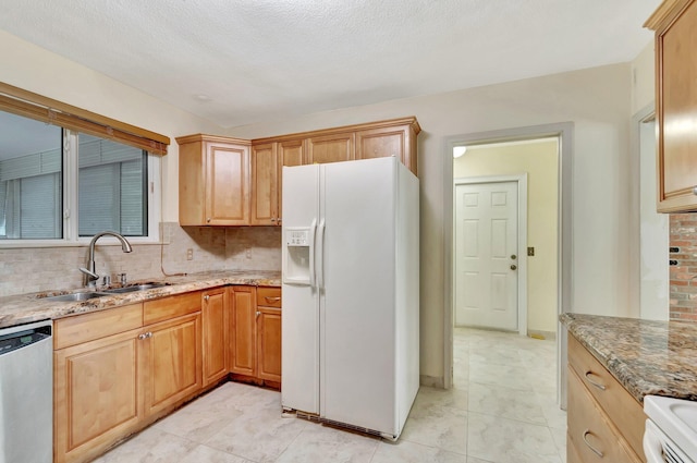 kitchen with light stone countertops, a sink, decorative backsplash, white fridge with ice dispenser, and dishwasher