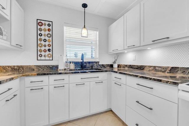 kitchen featuring backsplash, light tile patterned floors, dark stone countertops, white cabinets, and a sink