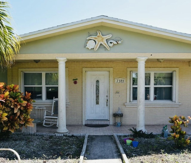 view of exterior entry featuring brick siding and a porch