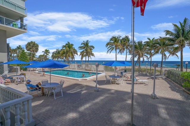 pool with a patio area, fence, and a water view