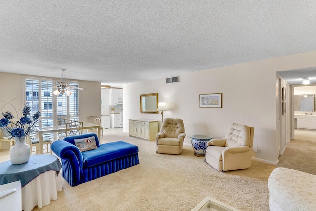 carpeted living area featuring an inviting chandelier, baseboards, visible vents, and a textured ceiling